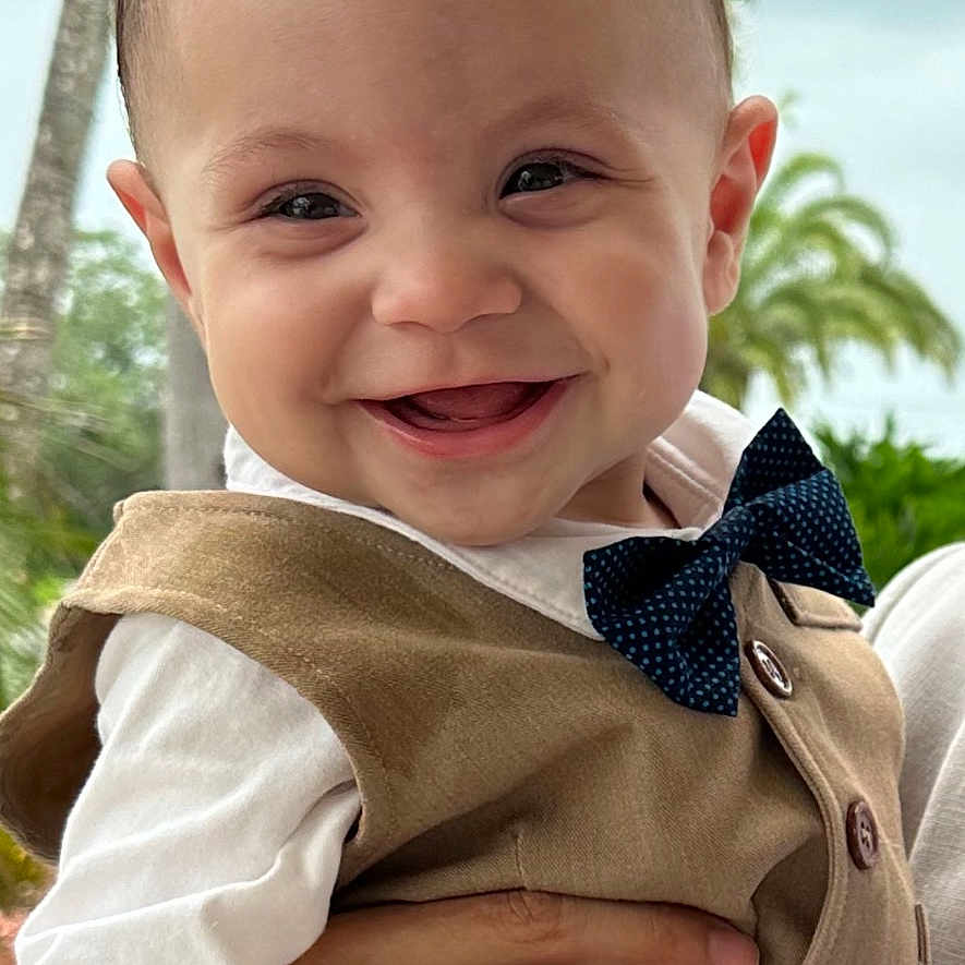 Wesley is registered to the contest to win money with this photo: accessories, baby, clothing, coat, face, formalwear, happy, head, jacket, laughing, palmtree, pants, person, photography, plant, portrait, shirt, smile, tie, tree