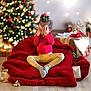 celebration, child, christmas_tree, cozy, cute, decorations, festive_bow, floor, gift_boxes, gold_pants, happy, holiday, indoor, lights, peekaboo, red_blanket, seasonal, smiling, socks, toddler