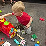 Ayden joined the competition — help win amazing prizes! toddler, child, toy_train, carpet, blocks, puzzle_pieces, red_shirt, gray_pants, indoor, playing, adult_legs, sneakers, couch, colorful_toys, learning_toys, floor, curly_hair, activity, person, game