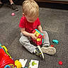 Ayden joined the competition — help win amazing prizes! toddler, child, toys, building_blocks, puzzle_pieces, carpet, indoor, sitting, playing, red_shirt, gray_pants, sneakers, adult_legs, couch, floor, colorful, blonde_hair, focused, casual_clothing, home