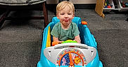 Ayden is registered to the contest to win money with this photo: blonde_hair, car, carpet, chair, child, cute, floor, furniture, green_shirt, indoor, person, plastic_toy, playful, room, shelf, smiling, toddler, toy_car, toys, young_child
