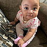 Ivey is registered to the contest to win money with this photo: baby, child, infant, sitting, couch, brown_couch, pink_clothing, socks, face, eyes, hand, necklace, patterned_clothing, indoor, portrait, cute, young, person, furniture, looking_up