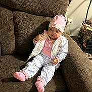 Ivey is registered to the contest to win money with this photo: baby, child, infant, pink_hat, pink_socks, jacket, pants, armchair, brown_furniture, indoor, home, relaxed, cute, cozy, seated, person, clothing, floor_lamp, basket, curious