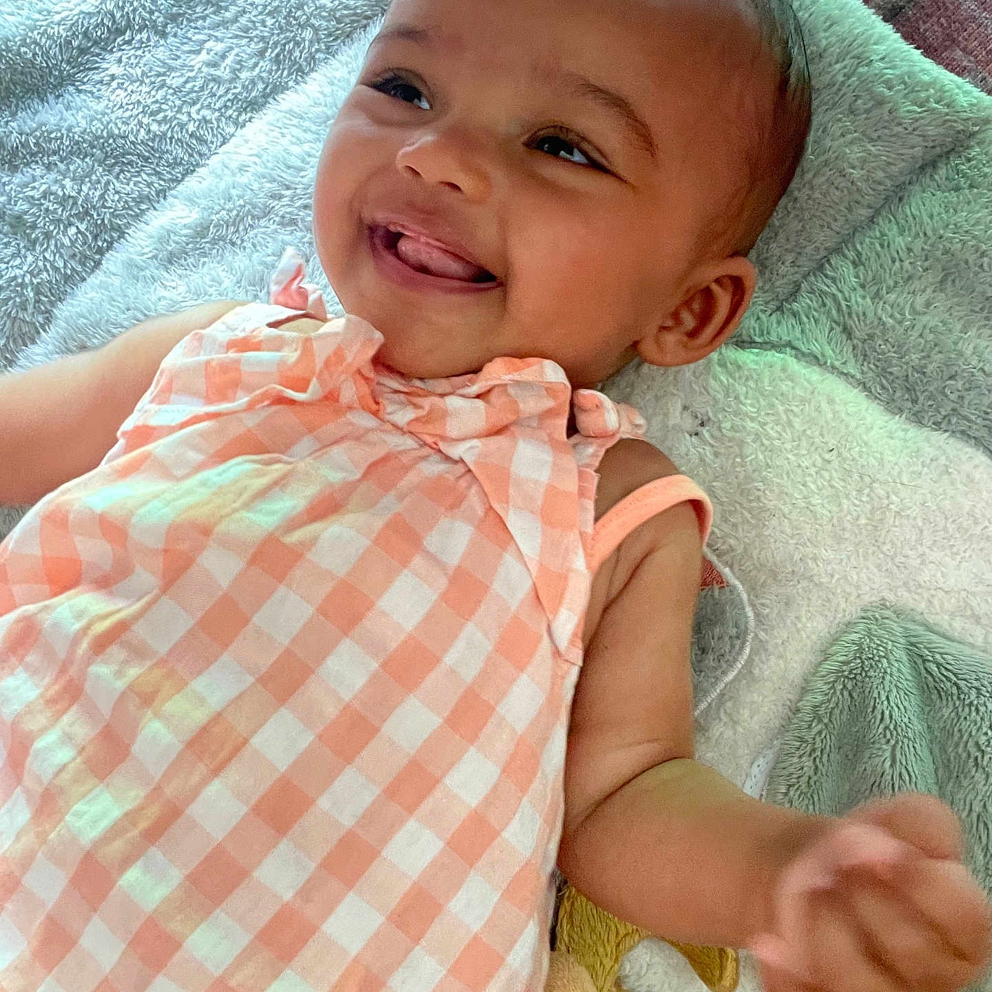 Safiya a rejoint le concours — aidez-le/la à gagner de superbes lots ! arm, baby, blanket, checkered_pattern, child, closeup, cute, dress, face, happy, indoors, infant, lying_down, peach_color, person, playful, portrait, skin, smiling, soft_texture