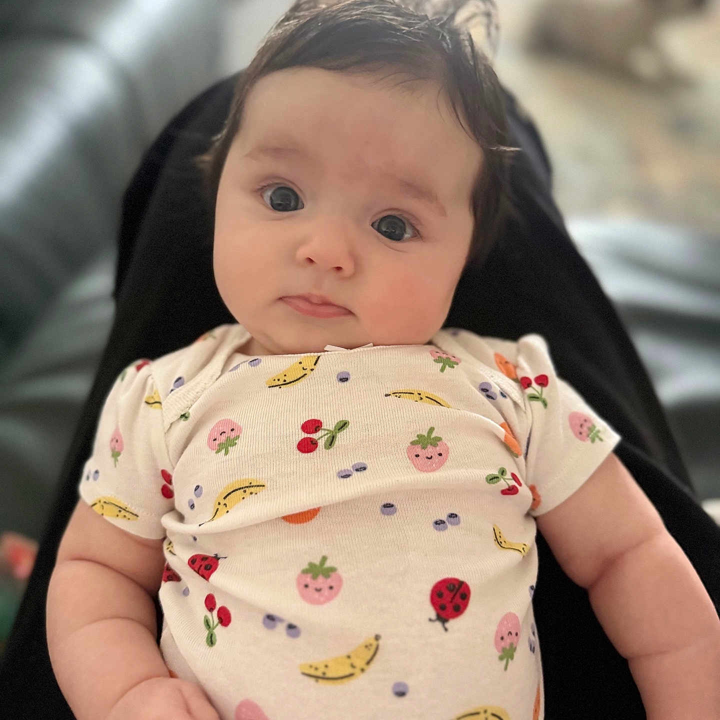 Eleanor is registered to the contest to win money with this photo: baby, background_blur, casual_clothing, child, chubby_cheeks, closeup, comfortable, curly_hair, cute, expression, fruit_pattern, hand, indoor, infant, ladybug, lying_down, onesie, person, skin, soft_light