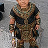 child, costume, aztec, feathers, headgear, armbands, concrete, street, traditional, cultural, footwear, toy, young, portrait, standing, outdoor, decorative, patterned, accessories, expression