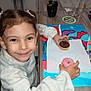 Anaïs a rejoint le concours — aidez-le/la à gagner de superbes lots ! brown_eyes, child, cute, donut, drink, face, food, glass, hair, happy, indoor, kitchen, person, pigtails, placemat, smiling, snack, sweater, table, white_clothing