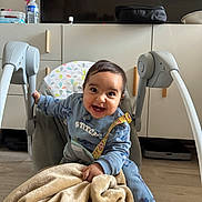 Aws participe au concours pour gagner de l'argent avec cette photo : baby, child, smiling, blue_clothing, blanket, baby_rocker, indoor, floor, cabinets, television, happy, person, toddler, toy_strap, cozy, cute, home, furniture, expression, casual