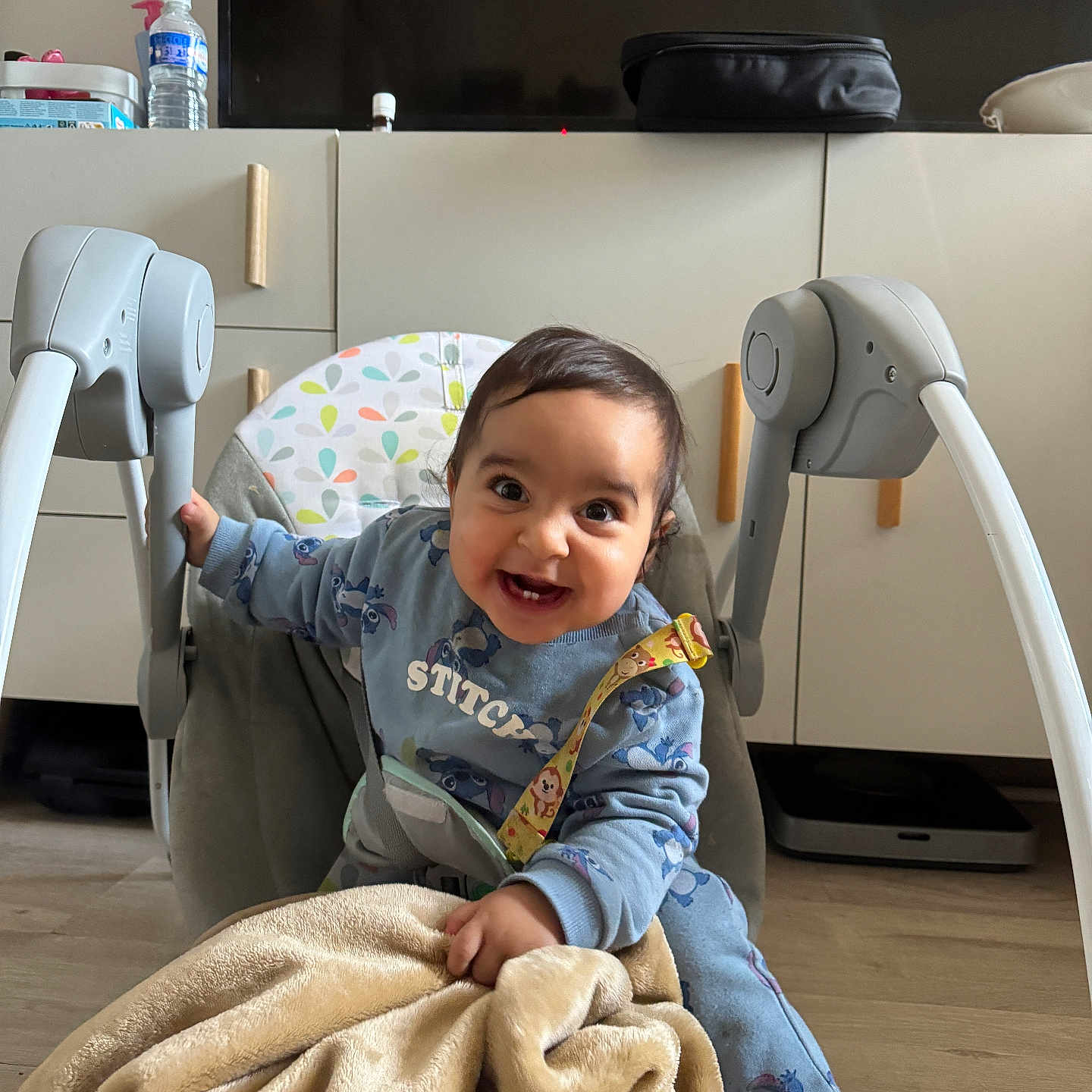 Aws participe au concours pour gagner de l'argent avec cette photo : baby, baby_rocker, blanket, blue_clothing, cabinets, casual, child, cozy, cute, expression, floor, furniture, happy, home, indoor, person, smiling, television, toddler, toy_strap