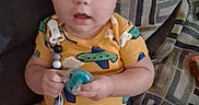 Brendon is registered to the contest to win money with this photo: baby, child, infant, onesie, pacifier, couch, patterned_cushion, indoors, sitting, curious, cute, plush, person, young_child, furniture, home, looking_at_camera, short_hair, bright_clothing, expression