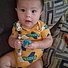 baby, child, infant, onesie, pacifier, couch, patterned_cushion, indoors, sitting, curious, cute, plush, person, young_child, furniture, home, looking_at_camera, short_hair, bright_clothing, expression