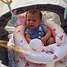 Brendon is registered to the contest to win money with this photo: baby, infant, stroller, inflatable_ring, toy, outdoor, sunlight, expression, child, clothing, blue_shirt, pink, white, playtime, cushion, seat, person, cute, summer, shade