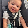 baby, smiling, car_seat, pacifier, infant, child, safety_harness, clothing, cute, hands, head, face, seat_belt, indoor, young_child, happy, expression, blanket, strap, person