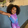child, girl, curly_hair, smiling, colorful_outfit, gym, indoor, wall, leaning, playful, earrings, casual_pose, young, happy, portrait, sport, athletic_wear, concrete_floor, lighting, cheerful