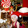 baby, child, santa_hat, red_overalls, sled, christmas_tree, holiday_lights, wooden_floor, indoor, festive, decorations, toy, crawling, cute, face, person, christmas, red_chair, plush, winter