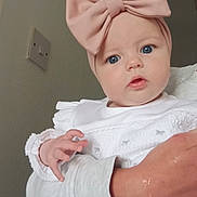 Rosa joined the competition — help win amazing prizes! baby, child, infant, headband, pink_bow, blue_eyes, white_clothing, hand, adult_arm, portrait, indoor, curious, cute, person, face, skin, sleeve, closeup, soft_light, neutral_background