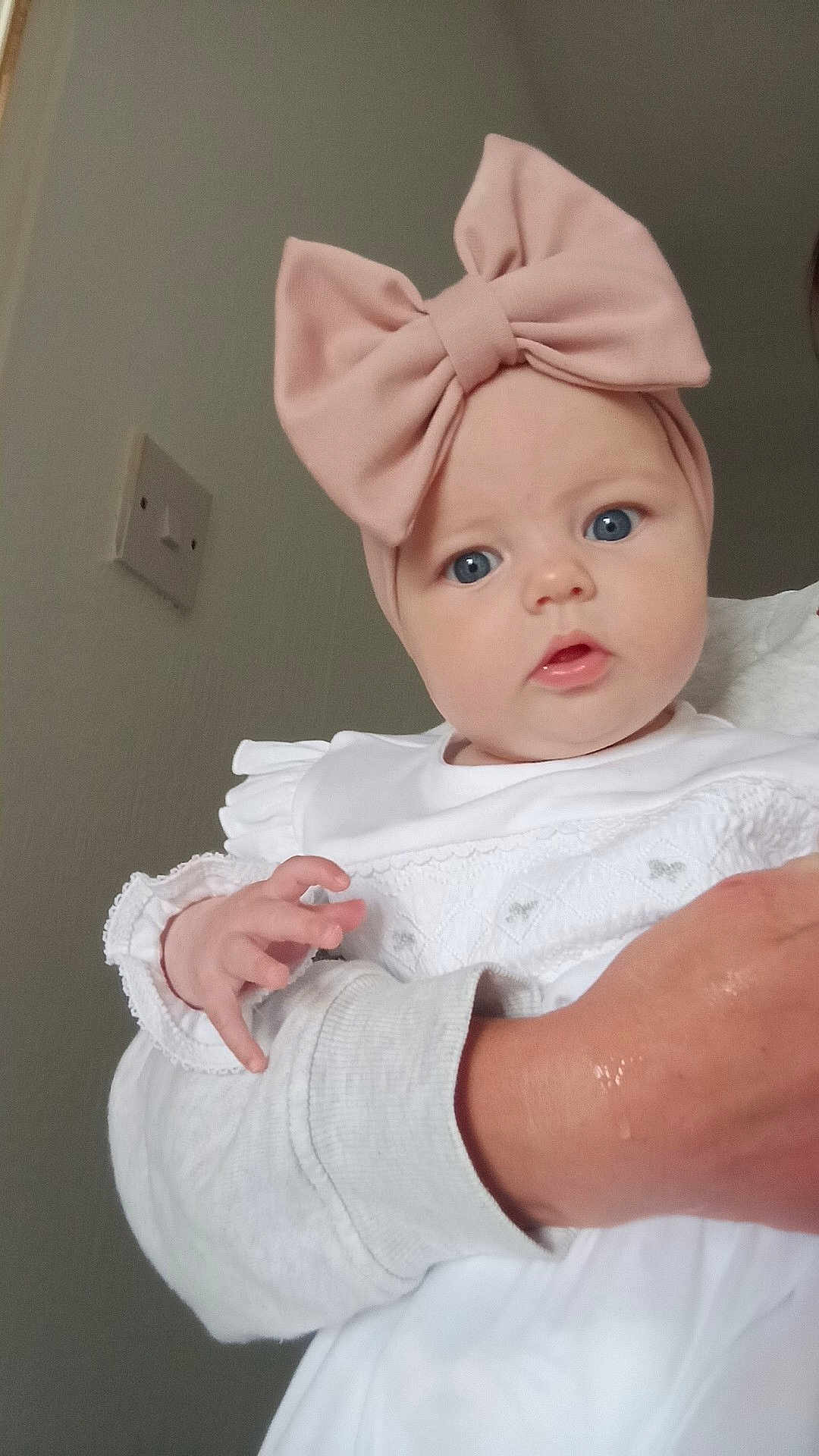 Rosa joined the competition — help win amazing prizes! baby, child, infant, headband, pink_bow, blue_eyes, white_clothing, hand, adult_arm, portrait, indoor, curious, cute, person, face, skin, sleeve, closeup, soft_light, neutral_background