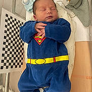 Kalel participe au concours pour gagner de l'argent avec cette photo : newborn, baby, sleeping, superhero_outfit, blue_clothing, hospital_bassinet, blanket, plush_toy, infant, cute, child, person, portrait, indoor, resting, soft_toys, clothing, peaceful, baby_garment, healthcare