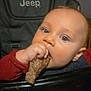 Waylon is registered to the contest to win money with this photo: baby, child, blue_eyes, meat, high_chair, jeep_logo, indoor, portrait, eating, hand, face, curious, young_child, seated, furniture, wall_art, closeup, skin, clothing, infant