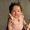accessories, baby, bottle, bracelet, child, couch, cute, face, gray_background, hair_buns, indoors, infant, pink_clothing, portrait, sitting, smiling, soft_lighting, strawberry_embroidery, striped_shirt, young_child