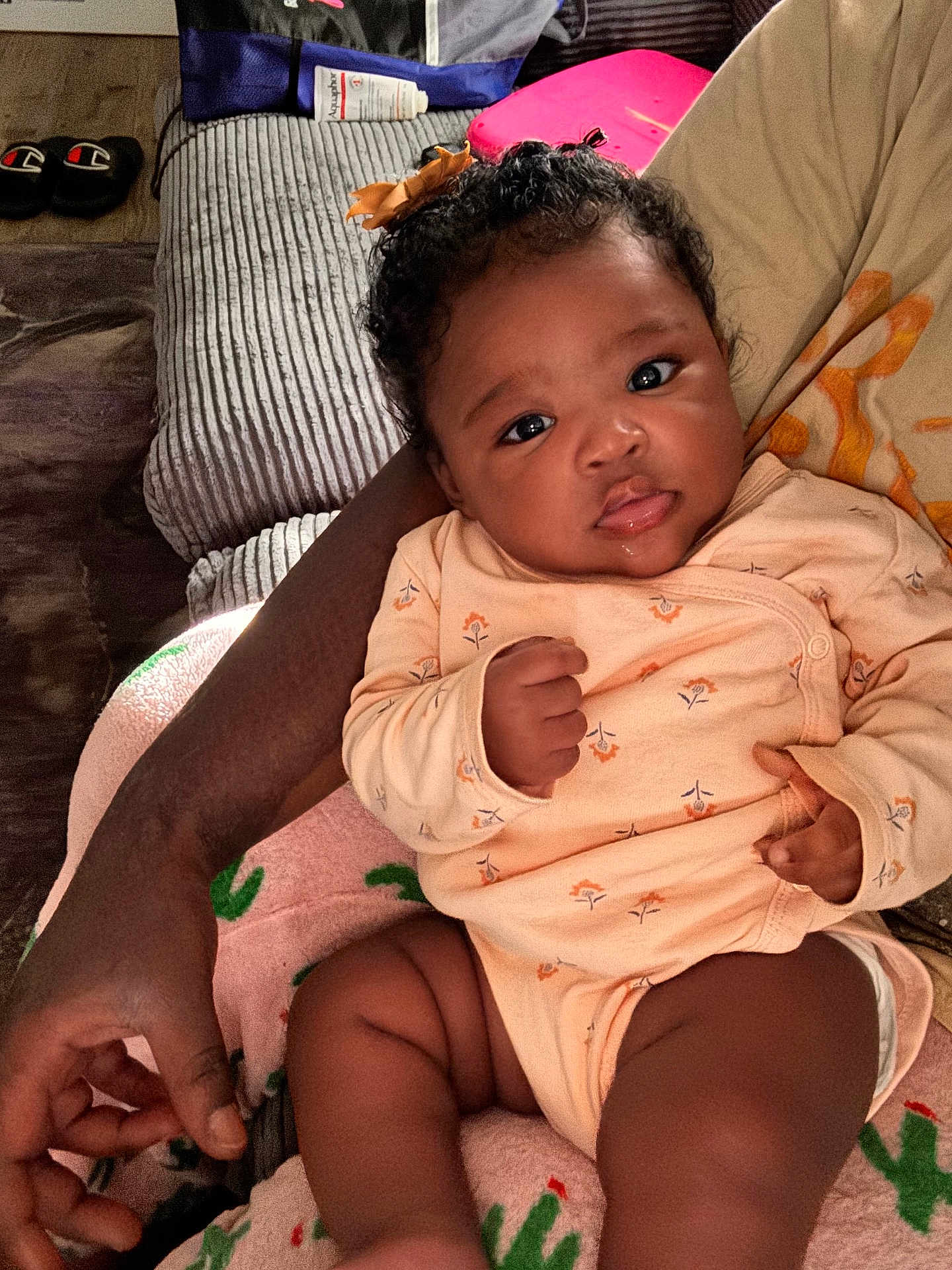 London joined the competition — help win amazing prizes! baby, infant, child, person, arm, hand, onesie, clothing, curly_hair, bow, drool, indoor, sofa, slippers, blanket, floral_pattern, skin, cute, resting, gaze