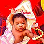 London is registered to the contest to win money with this photo: baby, infant, towel, pink, striped, pacifier, beads, face, arm, hand, curly_hair, expression, blanket, red_background, black_background, cloth, cute, newborn, child, portrait