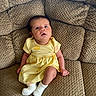 Oaklynn is registered to the contest to win money with this photo: baby, infant, yellow_dress, white_socks, couch, textured_fabric, seated, indoors, child, cute, curious, small, portrait, comfortable, relaxed, looking_up, skin, person, home, soft_lighting
