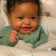 Olivia is registered to the contest to win money with this photo: baby, baby_seat, blanket, cheeks, close_up, curly_hair, cute, dimple, eyes, face, green_clothing, hand, happy, indoor, infant, newborn, pacifier, portrait, smiling, warm_lighting