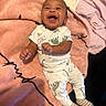 baby, smiling, laughing, infant, blanket, pink, dinosaur_print, clothing, striped_socks, cute, happy, lying_down, cozy, child, person, indoors, soft_texture, joy, expression, casual