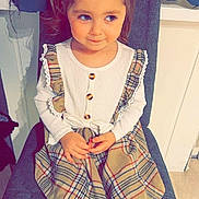 Stella participe au concours pour gagner de l'argent avec cette photo : child, girl, pigtails, plaid_dress, white_tights, black_boots, chair, indoor, smile, cute, sitting, long_sleeve_shirt, buttons, hands, floor, wall, furniture, portrait, young_child, happy