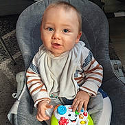 Shayron a rejoint le concours — aidez-le/la à gagner de superbes lots ! baby, child, infant, toy, game_controller, striped_clothing, bib, sitting, gray_chair, indoor, carpet, curious, blue_eyes, hand, face, smiling, young, cute, person, home