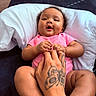 baby, infant, pink_clothing, hand, tattoo, pillow, couch, skin, smile, happy, child, cute, indoor, person, holding_hands, relax, comfort, portrait, young_child, human