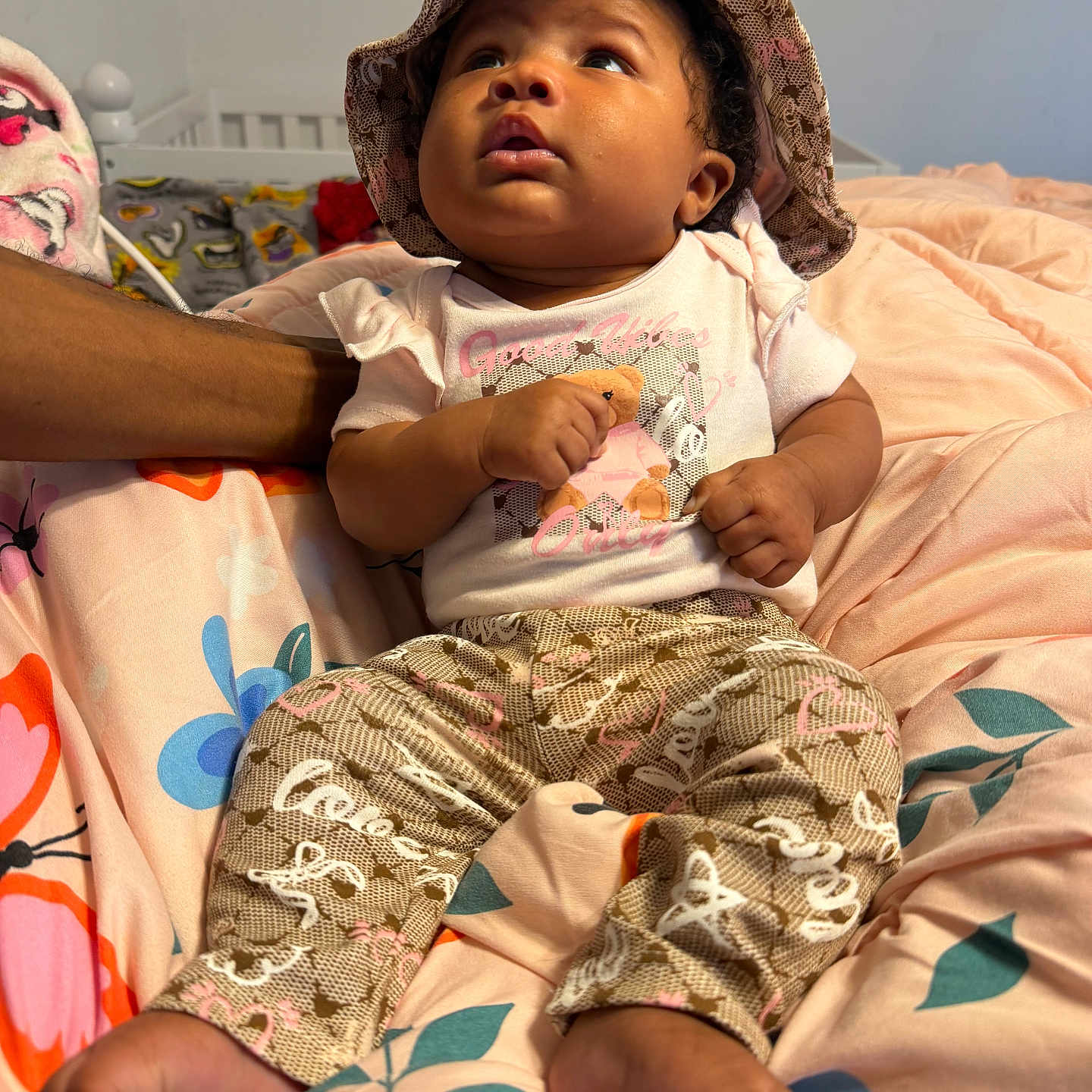 Zsamiya is registered to the contest to win money with this photo: baby, child, hat, pants, blanket, floral_pattern, bedroom, person, skin, hand, foot, clothing, infant, cute, sitting, indoors, support, looking_up, expression, resting