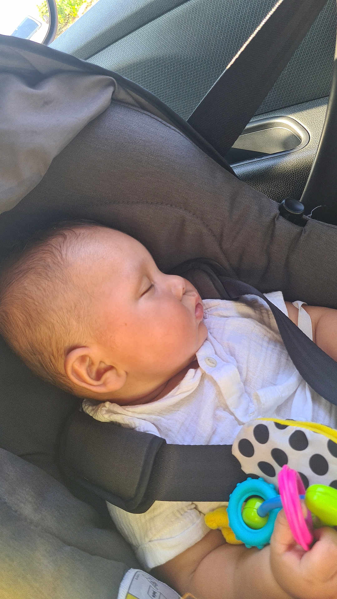 Zakarïa participe au concours pour gagner de l'argent avec cette photo : baby, car_seat, sleeping, child, toy, seatbelt, infant, car_interior, side_profile, clothing, white_shirt, peaceful, daylight, safety, cute, hand, polka_dot, colorful, closeup, transportation