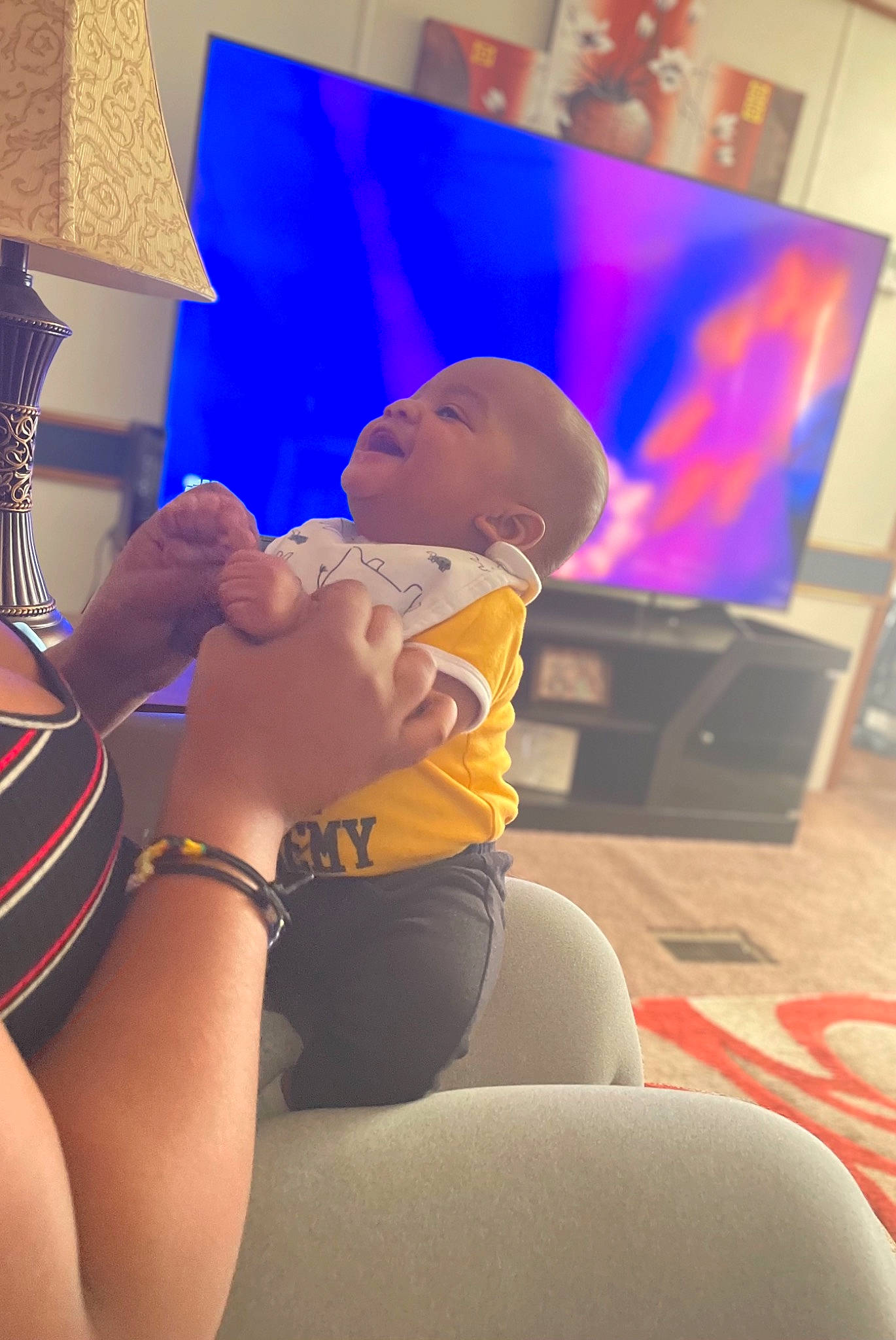 Jamarrion is registered to the contest to win money with this photo: baby, comfort, event, flat_panel_display, fun, happy, human_body, human_leg, interaction, knee, leisure, multimedia, person, purple, shorts, t_shirt, television, television_set, thigh, toddler