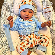 Gabriel is registered to the contest to win money with this photo: baby, infant, child, smiling, portrait, lying_down, bassinet, baby_bouncer, carrot_pattern, blue_clothing, hat, onesie, mittens, socks, raised_fists, indoors, wood_floor, cushion, happy, closeup