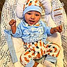 baby, infant, child, smiling, portrait, lying_down, bassinet, baby_bouncer, carrot_pattern, blue_clothing, hat, onesie, mittens, socks, raised_fists, indoors, wood_floor, cushion, happy, closeup