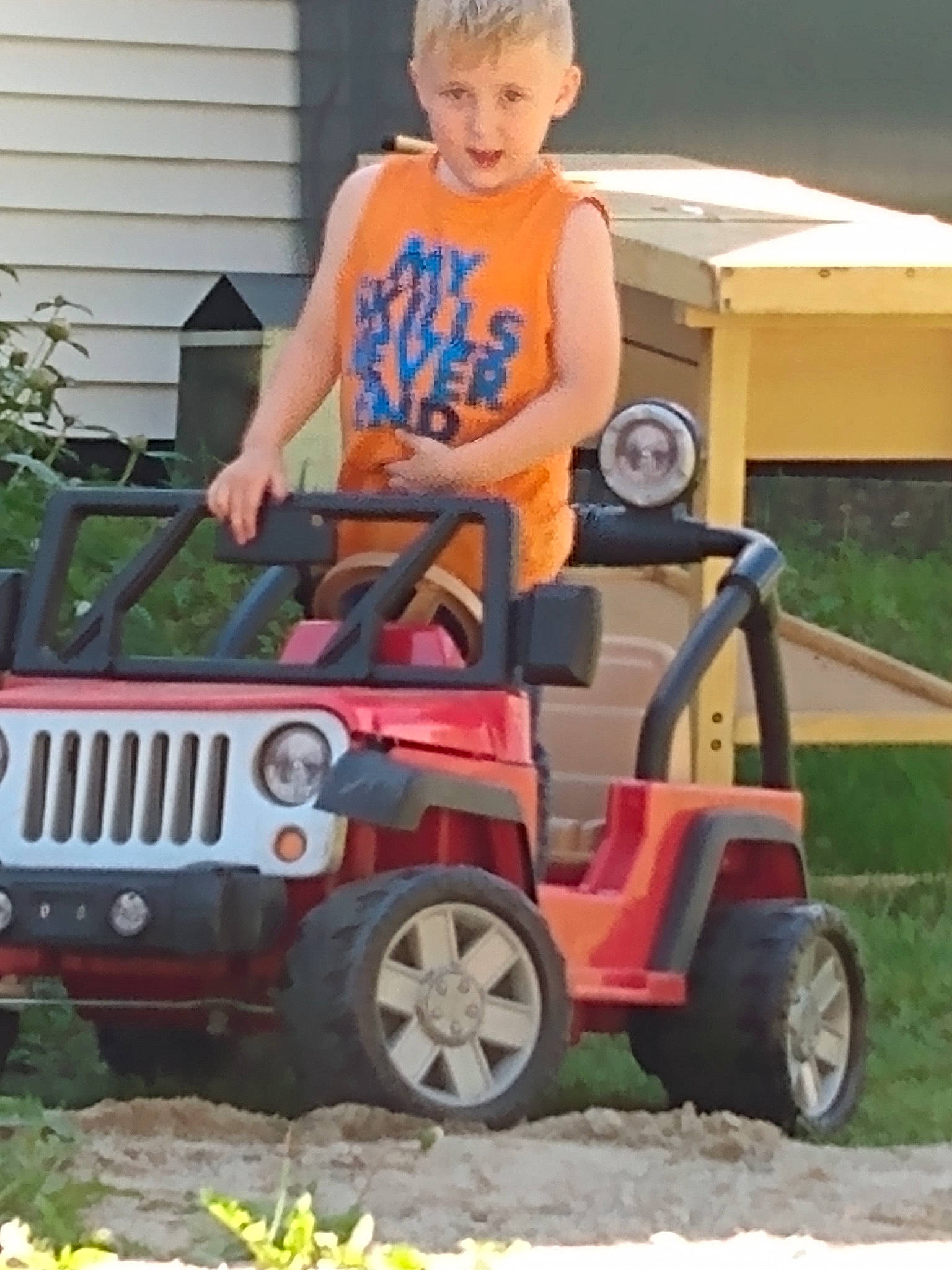 Jaden is registered to the contest to win money with this photo: automotive_design, automotive_exterior, automotive_tire, bumper, fender, grass, grille, hood, houseplant, motor_vehicle, person, plant, riding_toy, rolling, shorts, t_shirt, tire, toddler, tread, vehicle