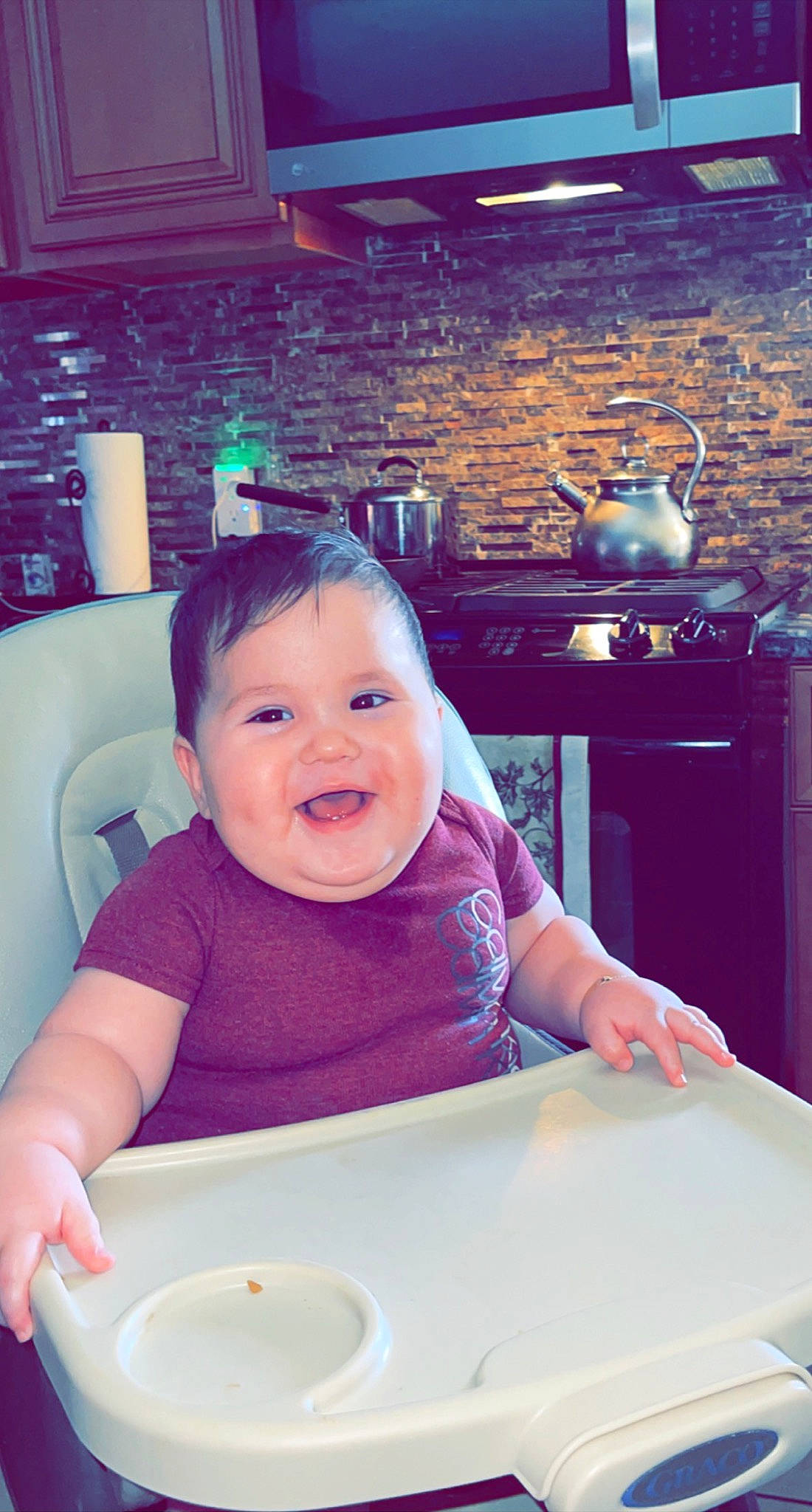 Gianni is registered to the contest to win money with this photo: baby, baby_toddler_clothing, cabinetry, child, countertop, dishware, gas_stove, happy, headwear, kitchen, kitchen_appliance, lighting, person, plate, purple, smile, snapshot, standing, t_shirt, table