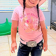 Zaela is registered to the contest to win money with this photo: child, girl, cowgirl, pink_hat, braids, smile, belt_buckle, cowboy_boots, jeans, t_shirt, indoor, blinds, tile_floor, playroom, happy, standing, portrait, accessory, playful, home_interior