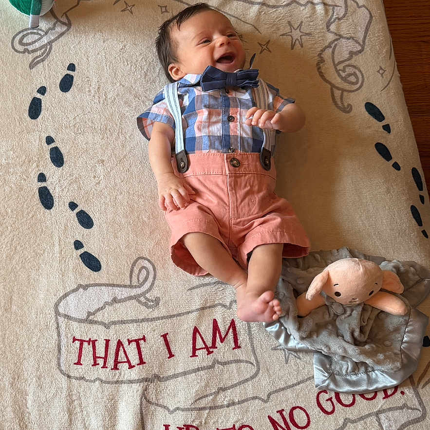Antony Romeo is registered to the contest to win money with this photo: baby, blanket, bow_tie, child, clothing, cute, face, floor, footwear, happy, indoors, infant, lying_down, playful, plush_toy, smiling, soft_toy, suspenders, toy, wood_floor