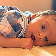 Antony Romeo is registered to the contest to win money with this photo: baby, infant, face, arm, plaid_shirt, clothing, skin, hand, lying_down, expression, eyes, soft_surface, close_up, indoor, child, portrait, young, cute, warm_light, reflection