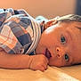 baby, infant, face, arm, plaid_shirt, clothing, skin, hand, lying_down, expression, eyes, soft_surface, close_up, indoor, child, portrait, young, cute, warm_light, reflection
