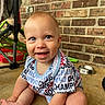 baby, child, smiling, sitting, onesie, blue_eyes, brick_wall, floor, stroller, metal_bowl, happy, cute, indoor, portrait, person, clothing, infant, face, baby_girl, baby_boy
