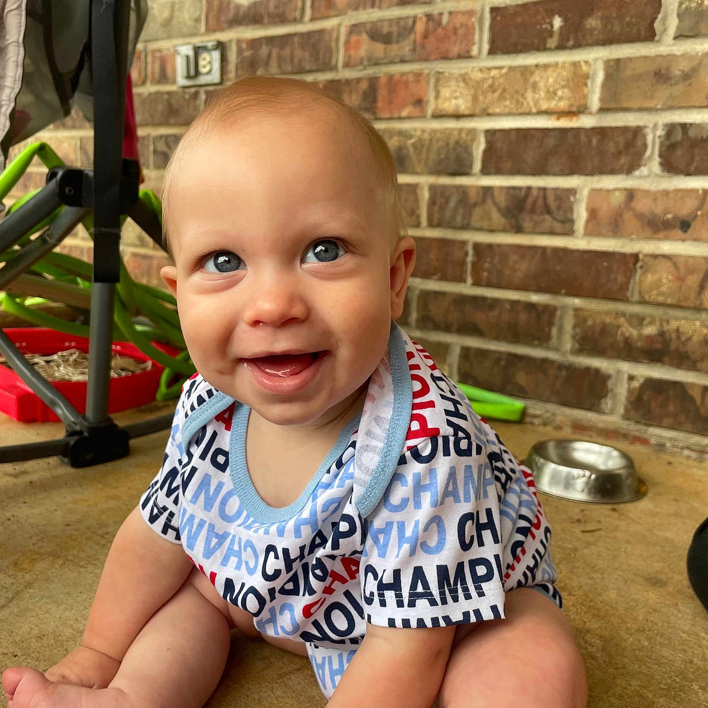 Zymani joined the competition — help win amazing prizes! baby, child, smiling, sitting, onesie, blue_eyes, brick_wall, floor, stroller, metal_bowl, happy, cute, indoor, portrait, person, clothing, infant, face, baby_girl, baby_boy