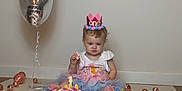 Lexi is registered to the contest to win money with this photo: balloon, birthday, cake, celebration, child, colorful_clothing, confetti, crown, cute, decorations, festive, indoor, number_one_candle, ornaments, party, sitting, smile, toddler, tutu, white_wall