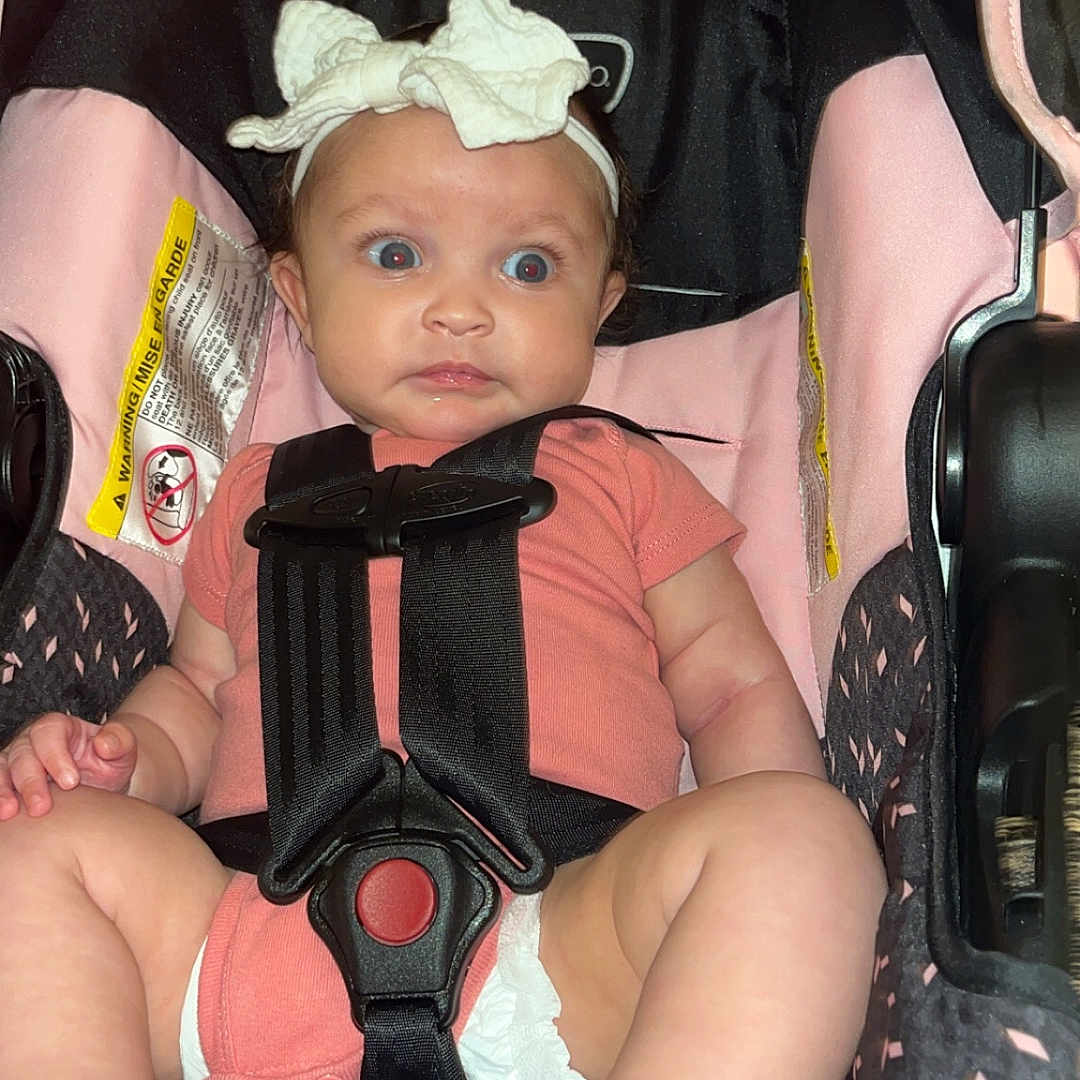 Laila joined the competition — help win amazing prizes! baby, black, car_seat, child, cute, diaper, expression, eyes, face, foot, headband, indoor, infant, leg, onesie, pink, safety, seat, sitting, straps