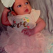 Laila is registered to the contest to win money with this photo: baby, infant, tutu, bow, headband, clothing, cute, love, pink, patterned_blanket, lying_down, soft_surface, portrait, child, small_hand, socks, gaze, adorable, indoor, young