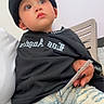 child, toddler, portrait, beanie, black_clothing, sweatshirt, jeans, ripped_jeans, sitting, indoors, chair, window, fashion, serious_expression, looking_up, face, eyes, person, casual_style, photography