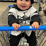 Sebastian joined the competition — help win amazing prizes! child, toddler, baby, smiling, happy, portrait, shopping_cart, supermarket, grocery_store, indoor, beanie, baseball_jersey, black_clothing, white_clothing, sneakers, cart_handle, sitting, shopping, shelves, retail